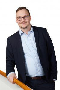 Kuvassa Sivistan elinkeinopoliittinen asiantuntija Jussi-Pekka Rode. Hän on tummahiuksinen ja hänellä on silmälasit. Hänellä on päällään tumma puku ja hän seisoo portailla kaiteeseen nojaten.